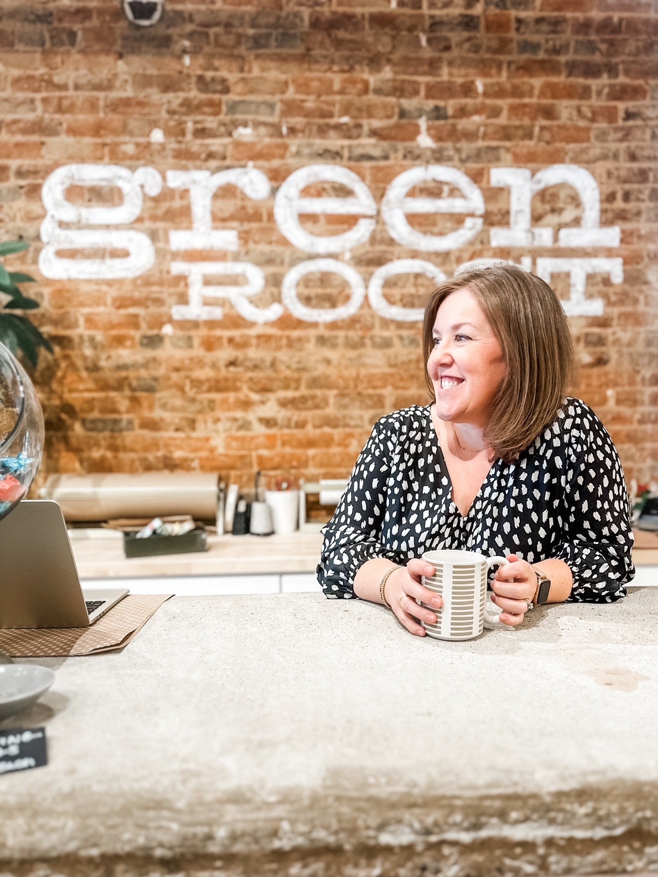 Woman sitting at a desk with a mug in front of a brick wall with 'Green Rocket' branding.